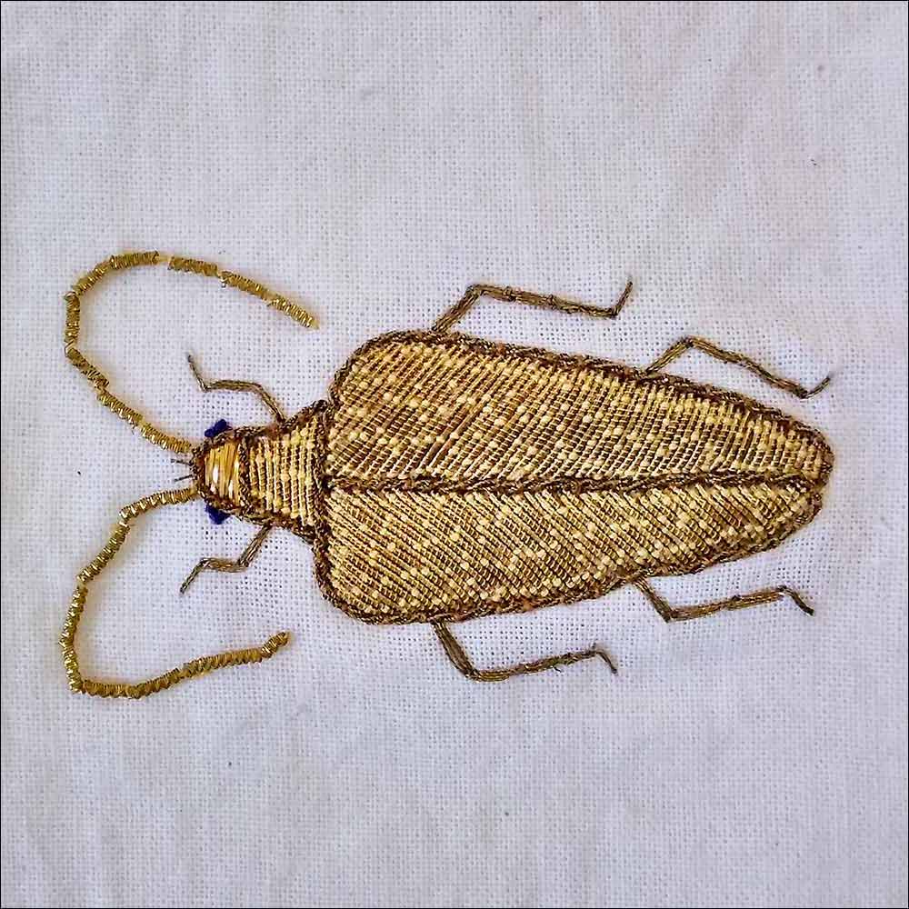 goldgestickter kaefer auf hellem stoff