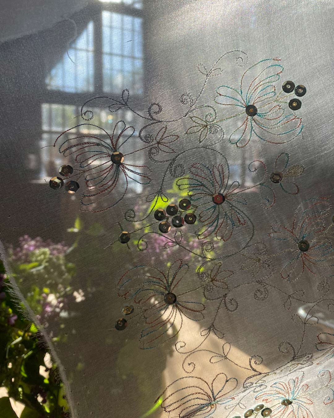Eine transparente Lunéville-Stickerei von Lisa Reichmann wird im Atelier Stark & Köppe vor lichtdurchfluteten Fenstern hochgehalten.
